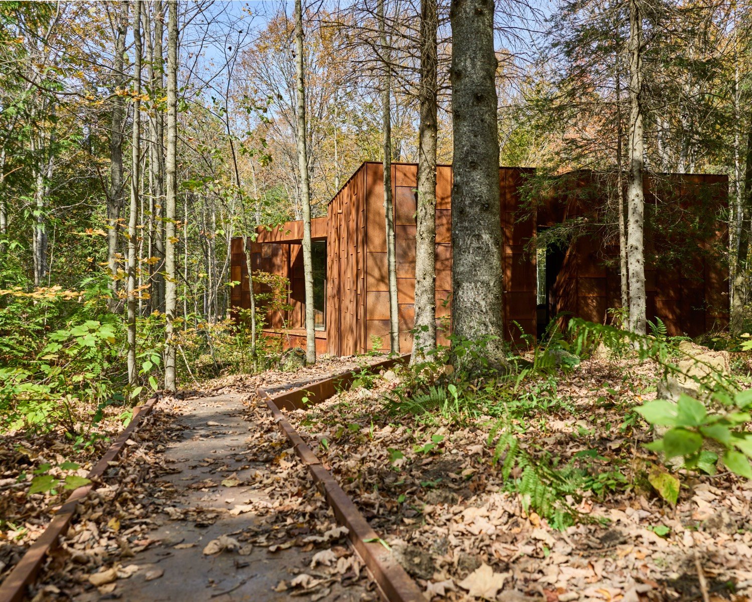 A Weathered Steel-Clad Artist’s Studio Recedes Into Its Forested Surroundings